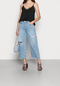 Camisola nera con bordo in pizzo abbinata a jeans a vita alta, larghi e di colore azzurro chiaro, con dettagli strappati e orli sfrangiati. Sandali neri con tacco.