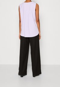 Vaaleanlila ilmanhiha toppi, jossa on pyöreä pääntie ja laskostus yksityiskohtana selässä, yhdistetty mustiin leveälahkeisiin housuihin. Matte-kankaan tekstuuri.