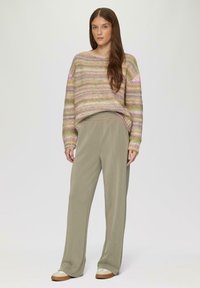 Brede trui met pastelstrepen in roze, groen en paars. Gecombineerd met lichtgrijze, ruime broek en beige sneakers.