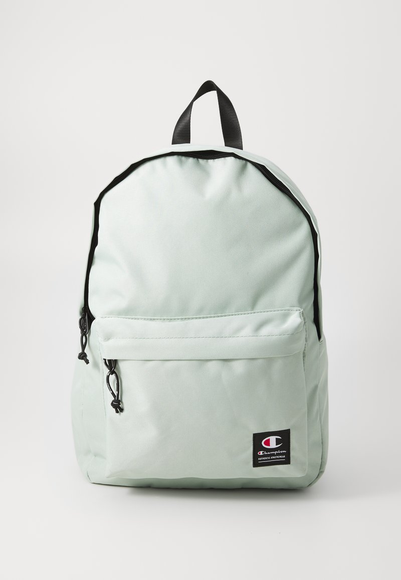 Sac à dos vert menthe muted avec une finition texturée, des accents noirs, une poche avant et une poignée supérieure pour le transport. Comprend un patch de marque.