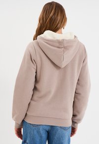 Felpa con fodera in pile color beige chiaro, con tasca frontale tipo kangaroo, maniche lunghe e polsini e orlo a coste. Dettaglio testurizzato sul colletto interno.