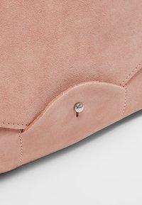Borsa in suede rosa grigio con una patta arrotondata, chiusura a scatto in argento e cuciture visibili lungo i bordi. Texture morbida.