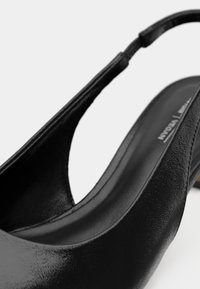 Μαύρο vegan δερμάτινο παπούτσι με λουρί στην πλάτη, με λεία υφή, ανοιχτό δάκτυλο και καμπύλη σιλουέτα που τονίζει τον μινιμαλιστικό σχεδιασμό.