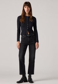 Zwarte lange mouwen, ribbeltop met ronde hals en knoopsluiting; gecombineerd met hoge taille zwarte jeans en enkellaarsjes; gladde stof, aansluitend ontwerp.