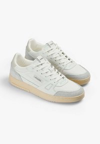 Zapatillas blancas que combinan lona suave y ante, con suela de goma beige y sutiles acentos de logo en el lado y en la lengüeta.
