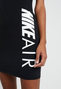 Svart klänning med en åtsittande design, med stor vit "NIKE AIR" text på sidan, tillverkad av ett mjukt, elastiskt material.