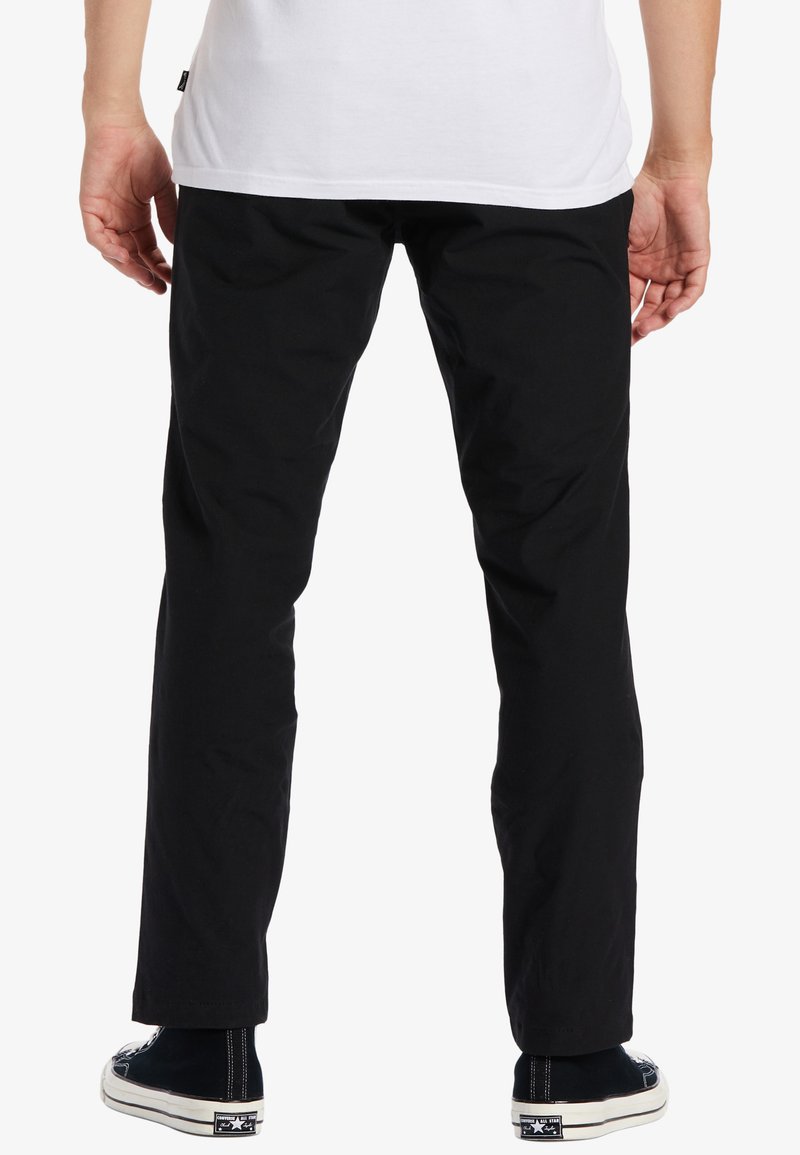 Pantalons en coton noir à coupe droite, avec une texture lisse et un minimum de détails, associés à des chaussures montantes noires.