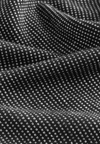 Tela negra con un patrón texturizado de pequeños cuadrados blancos. Textura suave y tejida con una superficie ligeramente elevada.