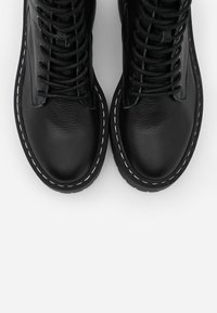 Black leather boots with a textured finish, featuring white stitching along the sole and laces, rounded toe, and high-top design.