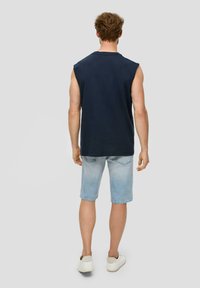 Marineblauw mouwloos shirt met ronde hals, gecombineerd met lichtblauwe denim shorts en witte sneakers, gezien van achteren.