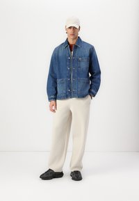 Jeans jakna u plavoj boji s dugmadima sprijeda, dva prednja džepa i detaljem s logom. Uparena s svijetlosmeškim hlačama i crnim teksturiranim teniskama.