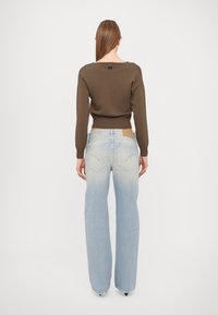 Pull marron avec ourlet côtelé et manches longues, associé à un jean bleu clair à jambes larges, présentant une décoloration et des détails sur la poche arrière.