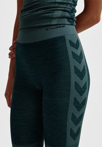 Hummel-teal tajta leggings med ett texturerat tyg och en kontrasterande midjeresår, som har ett sicksackmönster längs sidan för extra detaljrikedom.