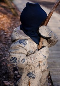 Beige padded snowsuit with blue mountain patterns, gray lining, and elastic cuffs; child holding a stick; navy blue hood and mittens.