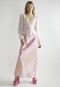 Blusa bianca con stampa floreale rosa, bordi in pizzo e maniche a sbuffo; abbinata a una gonna maxi in satin rosa ombré; indossata con tacchi alti rosa.