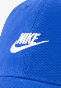 Blauwe baseballpet van stof met een gebogen klep, voorzien van een wit geborduurd "NIKE"-logo en swoosh aan de voorkant.