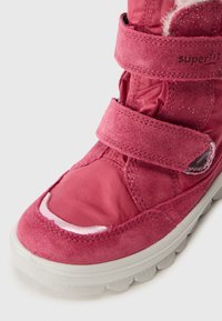 Rosa semsket og nylonstøvler med borrelåsremmer, med en teksturert tåhette og en hvit gummisåle. Glitterdetaljer på materialet.