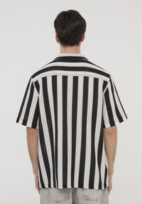 Camicia a maniche corte realizzata in tessuto a maglia, presenta strisce alternate nere e bianche, un colletto a punta e una vestibilità rilassata.