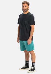 Svart bomull t-shirt med bröstficka; teal shorts; svarta sneakers med vita sulor; svarta strumpor med logotypdetaljer.