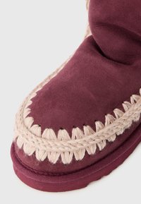 Stivale alla caviglia in suede bordeaux con un bordo intrecciato beige e dettagli a ondine, caratterizzato da una texture morbida e una punta rotonda.