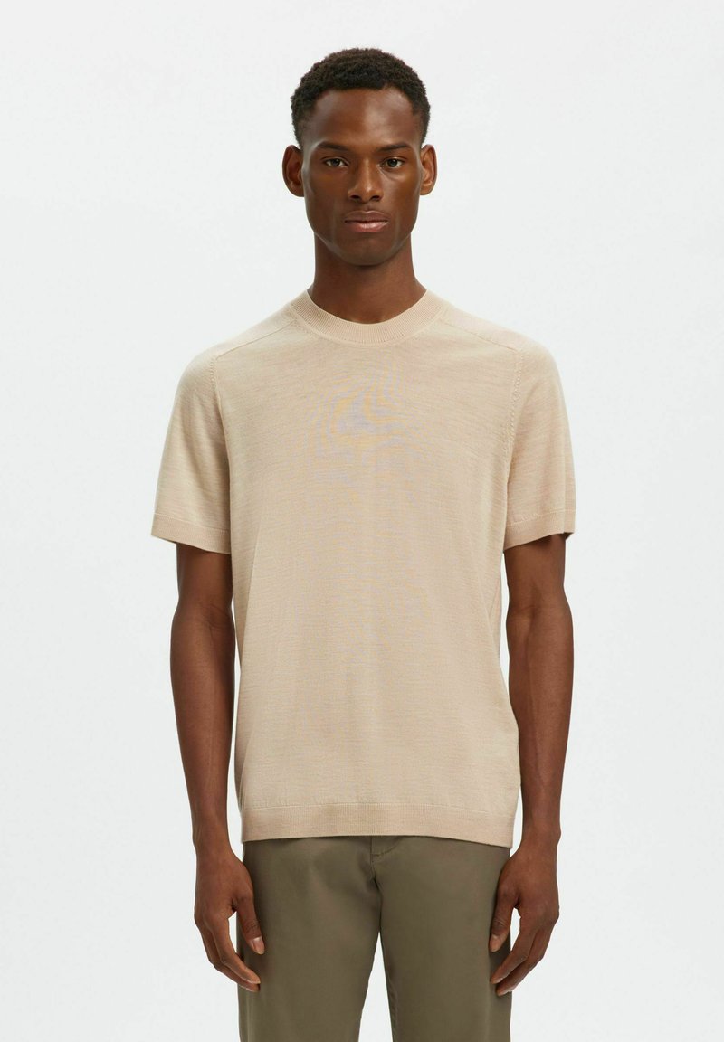 Chemise en tricot beige à manches courtes avec un col rond et des bords côtelés, fabriquée en matière légère, associée à un pantalon vert olive.