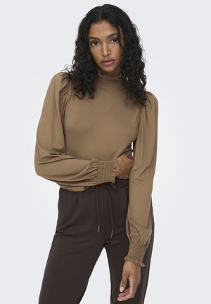 Top marrón de manga larga con un alto cuello con volantes y mangas abullonadas. Tejido suave con detalles fruncidos en los puños, combinado con pantalones oscuros.