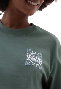 Zielona bawełniana koszulka z centralnym haftowanym wzorem w białym i jasnoniebieskim kolorze, z kątowym akcentem i okrągłym dekoltem.