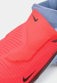 Crvena sintetička sportska cipela s teksturiranim gornjim dijelom, zakrivljenog oblika i svijetloplavim akcentima. Ima crni swoosh logo blizu pete.