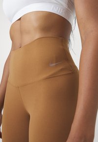 Visoke, uske tajice od smešnog materijala sa glatkom teksturom. Sadrže srebrni Nike logo sa strane.