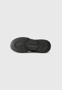 Black sneaker sole featuring textured rubber, a rounded shape, and a segmented design with grooves for traction.