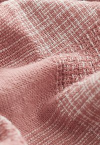 Tejido entrelazado en un tono rosa polvoriento, con un patrón de rejilla blanca texturizada, que presenta una apariencia suave y ligeramente difusa.