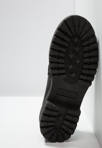 Semelle de botte noire robuste avec des crampons profonds, marque "ZIGN", taille 37, présentée sur fond blanc et contre un mur.