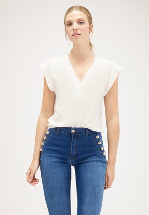 Witte V-hals blouse met kapmouwen, gecombineerd met blauwe high-waisted jeans met zijknopen en een gladde denimtextuur.