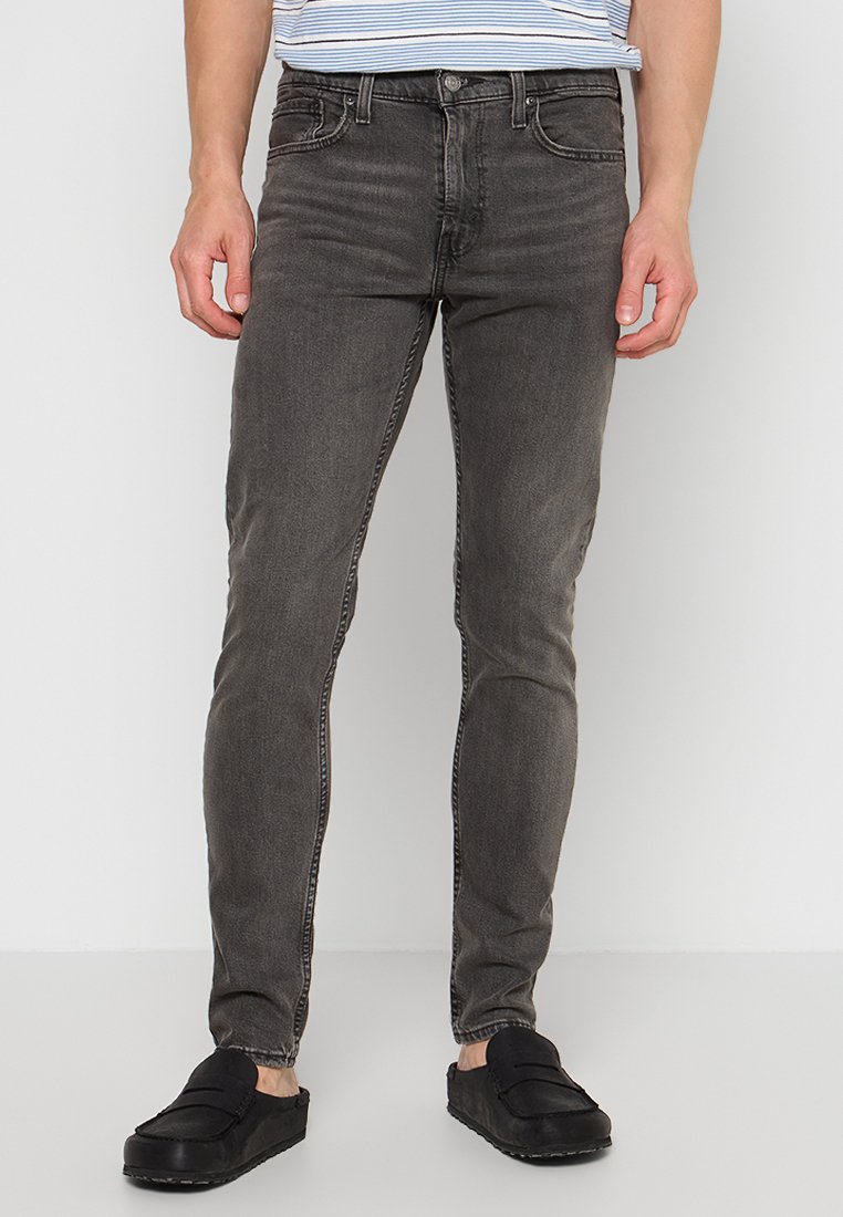 Schmal geschnittene graue Denim-Jeans mit einem verblassten Finish, fünf Taschen, Gürtelschlaufen und kontrastierenden Nähten. Getragen mit schwarzen Slippern.