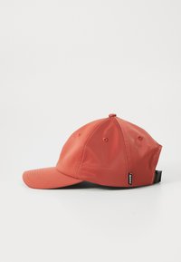 Vue latérale d'une casquette de baseball rouge avec une visière courbée et une sangle noire réglable à l'arrière, sur fond blanc.