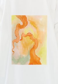 Witte t-shirt met een vierkant, abstract aquarelontwerp met oranje, geel en groene zwirls en gestructureerde penseelstreken.