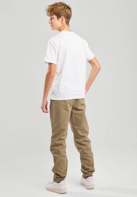Camiseta blanca de algodón con cuello redondo, combinada con pantalones cargo beige, de corte relajado y zapatillas blancas.