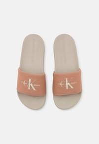Infradito con una fascia in tessuto pesca che presenta il logo bianco "CK" e un logo testurizzato su una suola in gomma beige. Design piatto e con punta aperta.