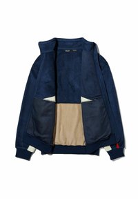 Marineblaue Jacke aus weichem Wildleder und Mesh, mit beigem Futter, Reißverschlusstaschen und gerippten Bündchen. Das offene Design zeigt die Details im Inneren.