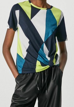 Camiseta multicolor con patrones geométricos en azul marino, verde lima, blanco y verde azulado. Manga corta, cuello redondo, detalle de nudo en la cintura.