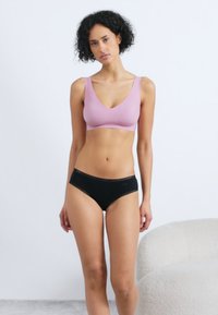Ljusrosa bh med breda band och v-ringad design, tillsammans med svarta hipsterunderbyxor med hål detaljer längs midjan.