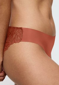Miedzieńskie majtki z gładkiego materiału z koronkowym akcentem w talii, prezentujące kwiatowy wzór i bezszwowe wykończenia.