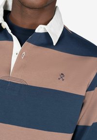 Maglietta da rugby con colletto, caratterizzata da righe orizzontali in blu navy e beige. Include un colletto interno bianco e un piccolo logo ricamato.