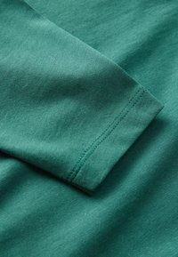 Blåt bomuldstof med en glat tekstur, udstyret med en opkrøllet ærmekant og en enkel sidesøm, der fremviser et subtilt, ensartet udseende.