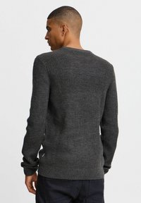 Dark gray knit sweater with a ribbed texture, long sleeves, and a rounded neckline. Features side slits and a fitted bottom hem.