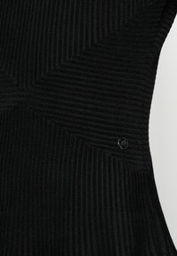 Μαύρο ριγωτό ύφασμα με γεωμετρικό σχέδιο, που διαθέτει μια μικρή λογότυπη προφορά. Λείος υφή με κατακόρυφες γραμμές; εφαρμοστή σχεδίαση.