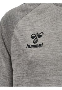 Grå melange sweatshirt med tekstureret stof, der har et sort logo på venstre bryst. Designet inkluderer raglanærmer.