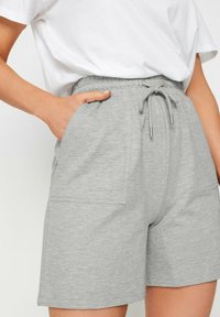 Shorts en coton gris avec une taille élastique, un cordon de serrage et deux poches latérales. Texture lisse avec un design décontracté.