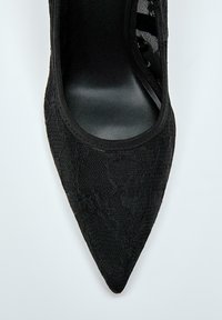 Črne visoke pete z ostro konico, ki imajo teksturiran čipkast premaz, gladko notranjost in enotno črno zunanjost s sleek oblikovanjem.