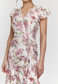 Robe portefeuille florale en tissu léger avec un motif aquarelle rose et vert, manches courtes bouffantes et détail de ruché sur le côté.